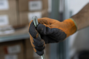 Mano con guante sosteniendo una varilla roscada usada para construcción, detalle, horizontal