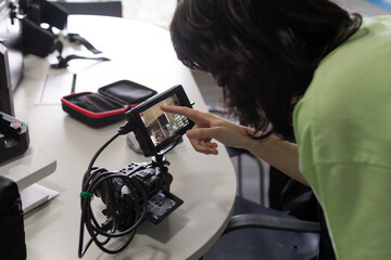 Mujer joven configurando cámara en monitor para filmar. Imagen horizontal, mesa con elementos de...
