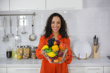 A Beautiful Smiling and happiness fit African American woman showing a bowl fruits in her kitchen....