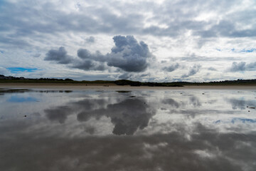 Reflets de gros nuages gris menaçants sur le sable mouillé d'une plage de la presqu'île de Crozon, une atmosphère saisissante et chargée d'émotion.