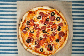 Top view of pizza with pepperoni, olives and tomato slices on craft paper on the table