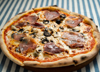 Traditional Italian pizza with bacon and mushrooms, cut into slices, close-up. Italian pizzeria