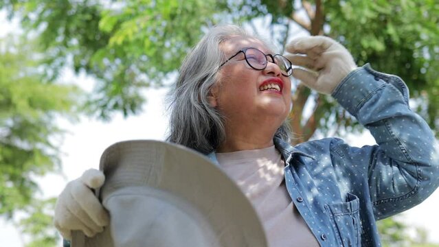 An elderly female farmer wearing glasses stands under a tree to avoid the sun. Extremely hot weather causes heat stroke.