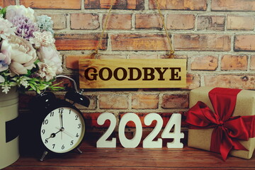 Goodbye 2024 letters with alarm clock and gift box on wooden background