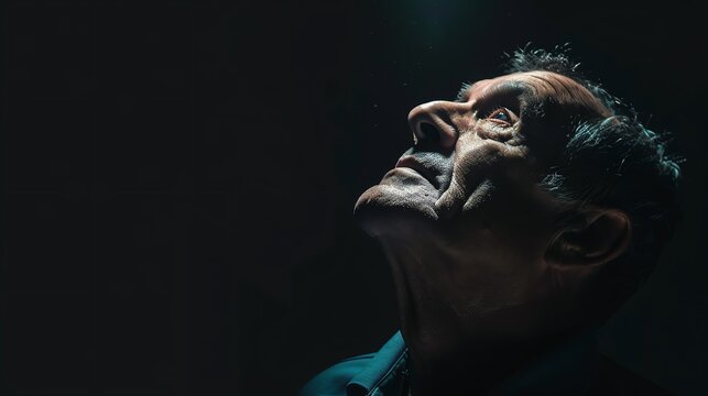 man look up with light illuminating his face on dark background.