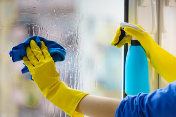 Gloved hand cleaning window rag and spray