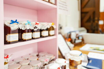 Shallow focus of a jar of homemade jam seen together with a collection of other jams located on a pink wooden display shelf within an English church.