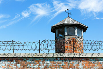 Historic brick prison wall showing guard tower and coiled barbed wire

