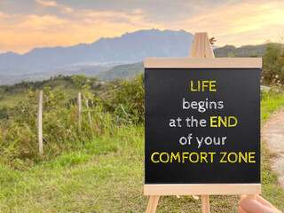 Inspirational motivating quote - life begins at the end of your comfort zone on chalkboard with nature background.
