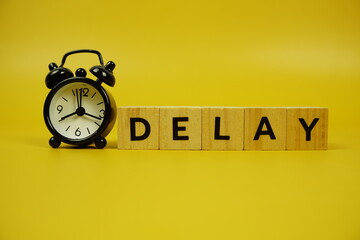 Delay with wooden blocks alphabet letters and alarm clock on yellow background