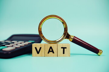 VAT with wooden blocks alphabet letters and Magnifying glass and calculator on blue background