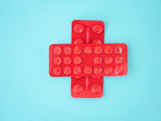 A red cross made of empty pill blisters on a blue background, a place for text. Treatment of...