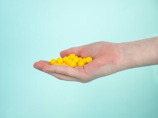 Round yellow tablets or biologically active vitamin supplements in the palm of a child on a blue...
