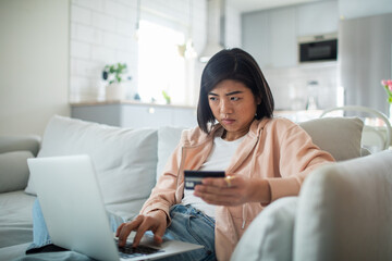 Young asian woman online shopping and making an online payment with her credit card on the couch on the laptop