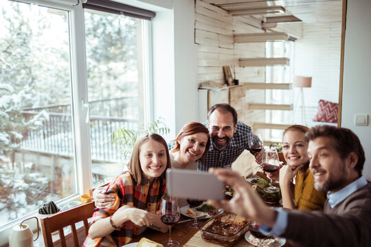 Friends taking a group selfie during a cozy winter meal indoors