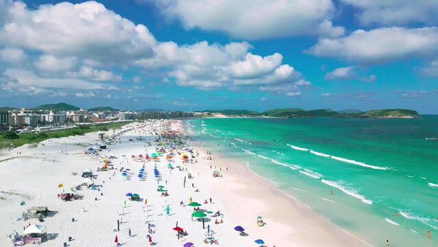 Aerial view of crowded white sand beach Cabo Frio, emerald coast filled with people with azure sea in Arraial do Cabo, Rio de Janeiro, Brazil.