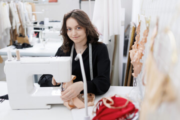 Seamstress woman in casual wear sit behind table using sewing machine, making modern lingerie