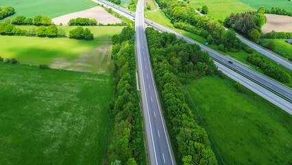 Drone view of a highway in Germany with a lot of traffic and many green fields around it.