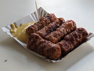 Mici cu mustar and a toothpick on a paper plate. Traditional romanian fast food. 