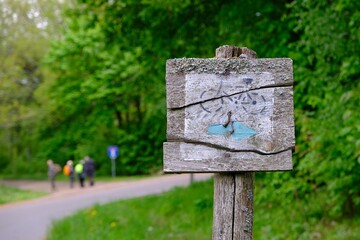 Old wooden sign of  bicycle trail and group of hiking people on road in background
