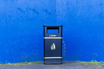 Black litter bin against blue wall in Glasgow