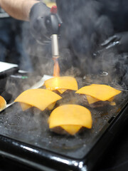 chef using kitchen torch to melt cheese on burgers