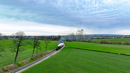 Dramatic aerial capture of a vintage steam train chugging along a curvy track through lush green...