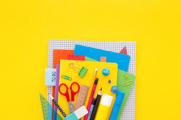 Stack of notebooks and school supplies on yellow background. Top view.