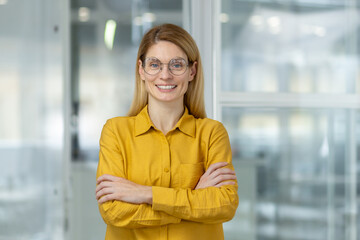 Portrait of a cheerful, confident businesswoman wearing a bright yellow blouse and glasses,...