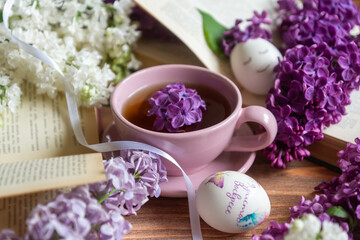 Easter and eggs with painting Christ is Risen, a cup of tea and lilac flowers, spring still life.