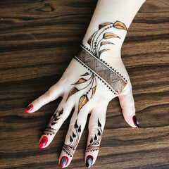 Striking henna tattoo on hand featuring detailed feather and geometric designs with glossy red nail...