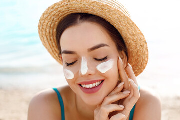 Beautiful woman applying cream sunscreen on a tanned face. Sunscreen. Skin and body care. The girl...