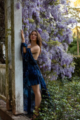 Attractive woman in blue dress near blooming wisteria. Ancient building