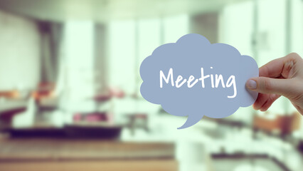 White "Meeting" text on blue bubble. Blurred office image in the background - Powered by Adobe