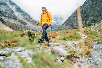 Man with backpack and trekking poles crossing mountain creek during Makalu Barun National Park trek in Nepal. Mountain hiking and active people concept image.