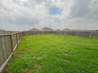 Suburban House Large Backyard with Wood Fence on a Cloudy Sky, Grass Maintained.