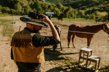 Cowboy standing near fenced grazing and taking care of his horses.