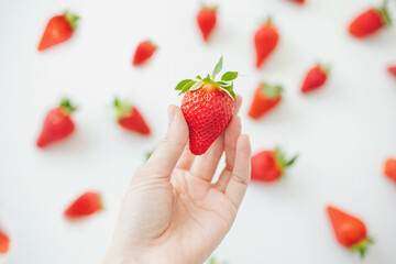 strawberry in hand on white background. a hand picking strawberries from a white surface. 