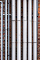Large and smaller silver pipes on a house wall with red bricks.