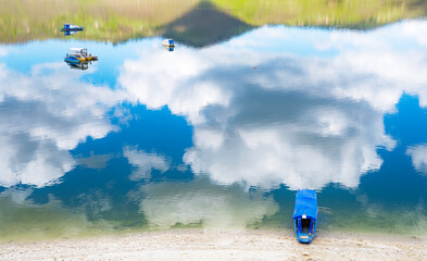 Lanscape image of boat floating on crisp mountaing lake water covered by cloud reflexions.