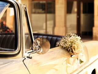 Detail of a white classic car with a bridal bouquet. Romantic vintage wedding car with flowers