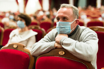 Mature man in antivirus mask in theater watching a performance