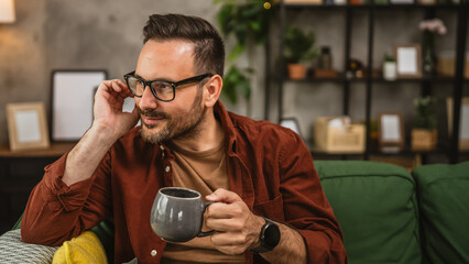 Adult caucasian man sit on sofa bed at home and hold cup of coffee
