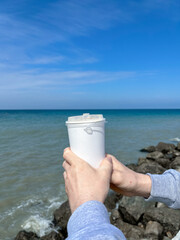 male hands holding a white plastic cup on the background of the sea