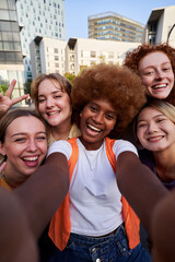 Vertical image of multiracial female friends taking a selfie with a smartphone outdoors. Cheerful young women smiling together looking at the camera enjoying the weekend outside in the city.