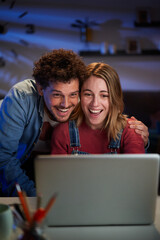 Vertical excited young adult Caucasian couple looking at laptop surprised celebrating successful start-up business. Millennial man and woman happy with positive results of online work at night home 