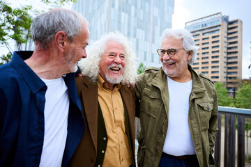 Group of three mature caucasian men enjoying embracing walk together laughing outdoor. Senior male old friends having fun hugging strolling happy in the urban city street. Elderly people golden ager