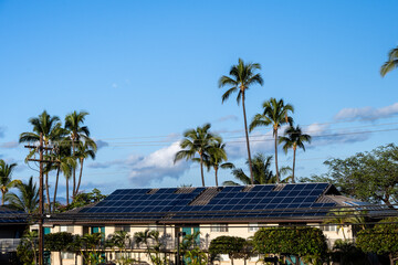 Condo building roof covered in solar panels to generate green alternative energy on sunny Maui, in...