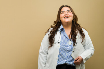 Smiling plus-size woman in medical attire with clipboard on a beige background