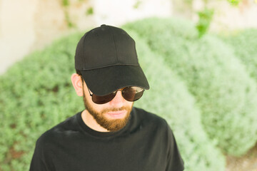 Hispanic man wearing sunglasses and a plain black t-shirt and cap stands for a perfect t-shirt and hat mock-up image